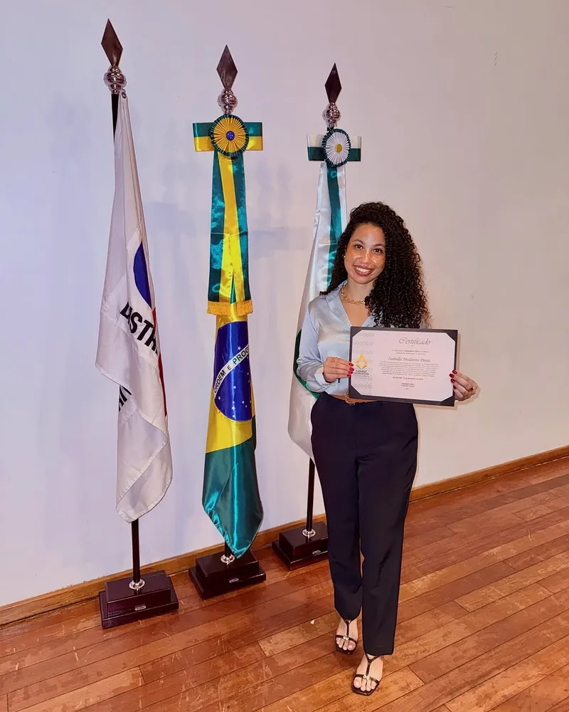Isabella Diniz segurando o certificado, ao lado das bandeiras, na Câmara Legislativa
